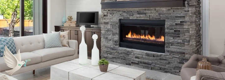Modern living room with stone fireplace and linear gas fire, beige sofa, decorative vases, and large window view of greenery.
