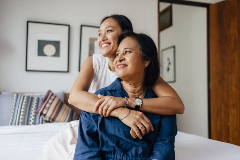 A smiling female embracing her mother while they are looking away.